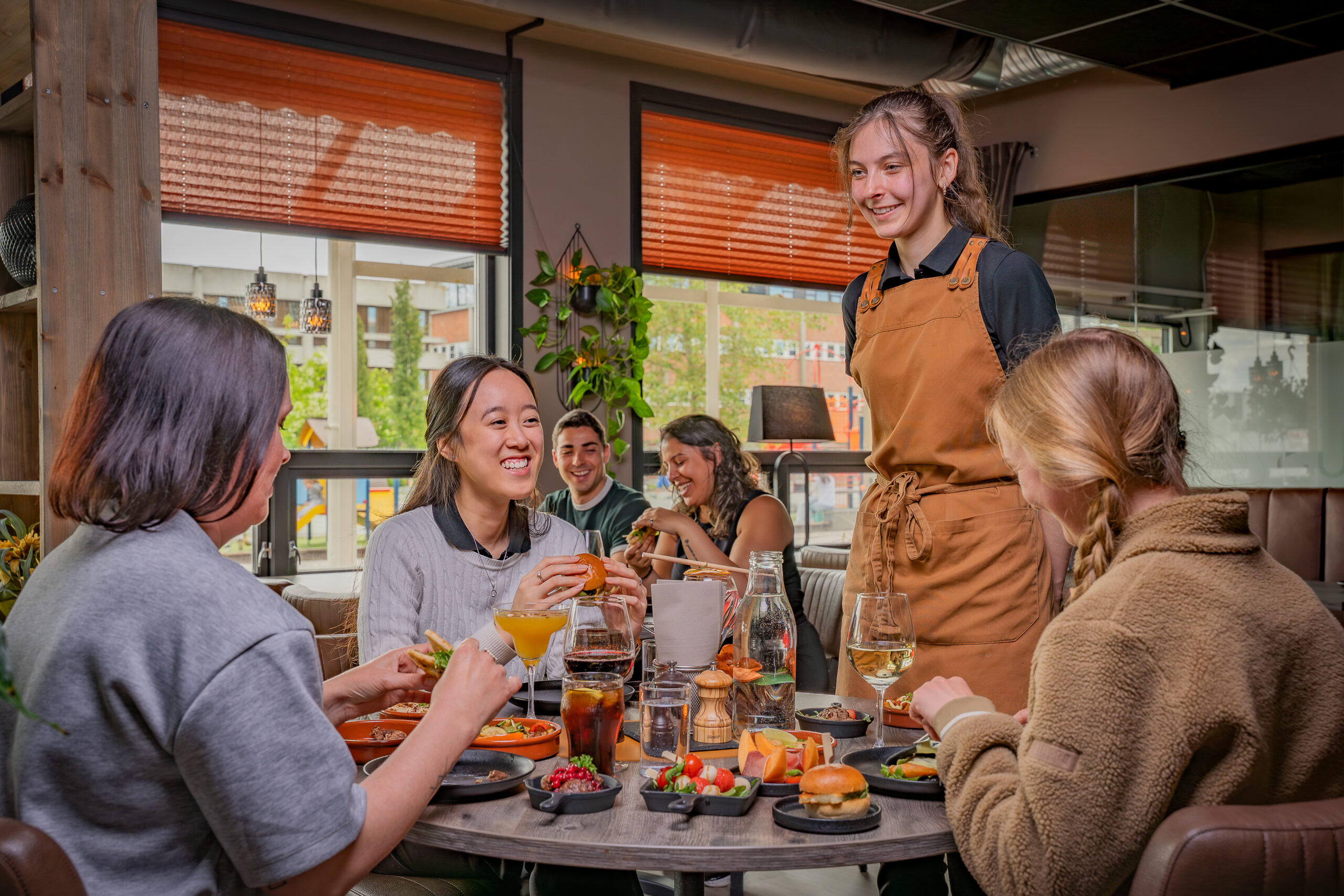 personer sitter rundt et bord og spiser, servitøren står ved siden av