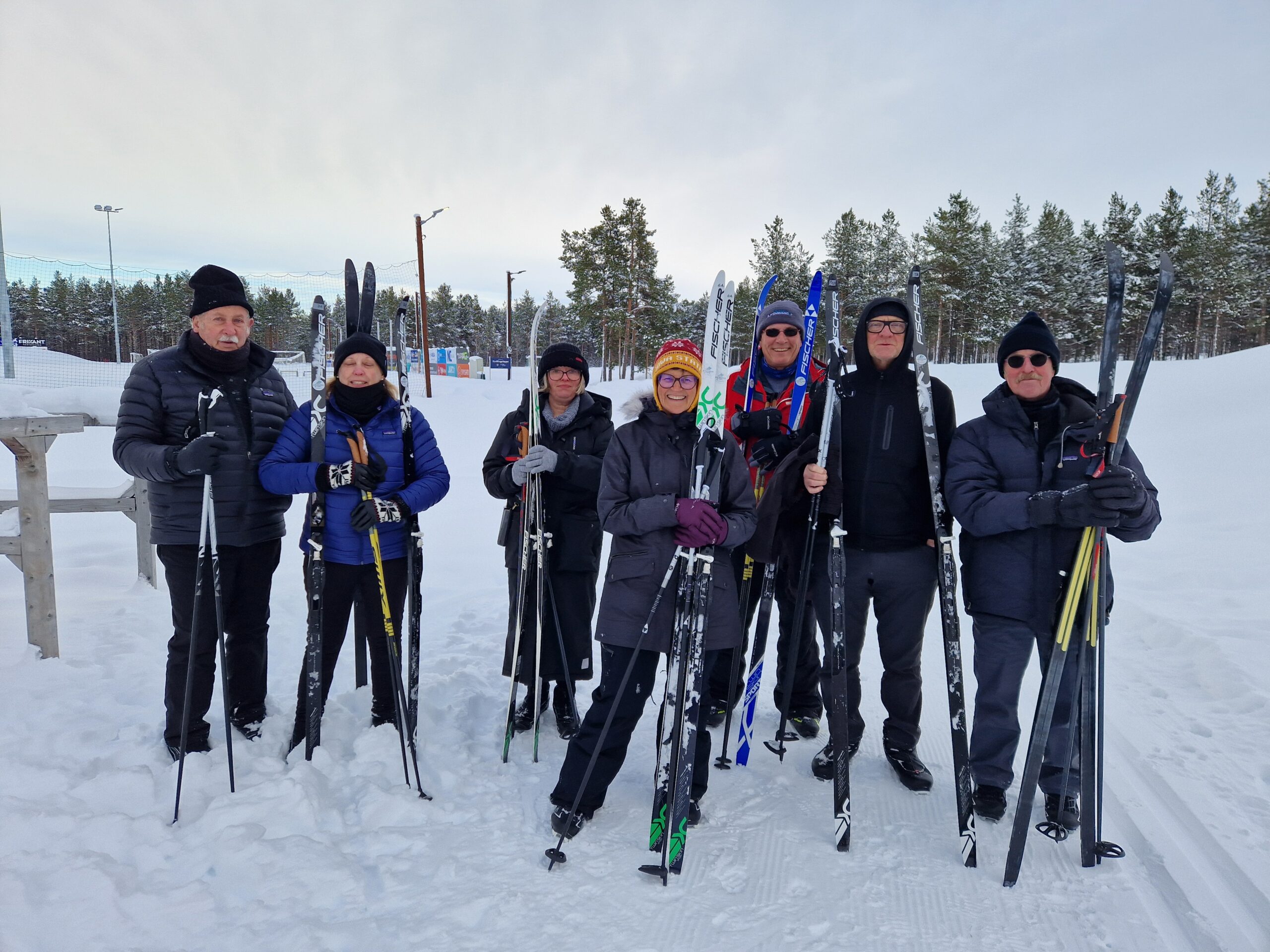 7 personer med ski står foran snøkledd skog